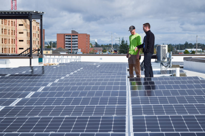 two people stand talking while looking at residential solar panels on the roof of a building