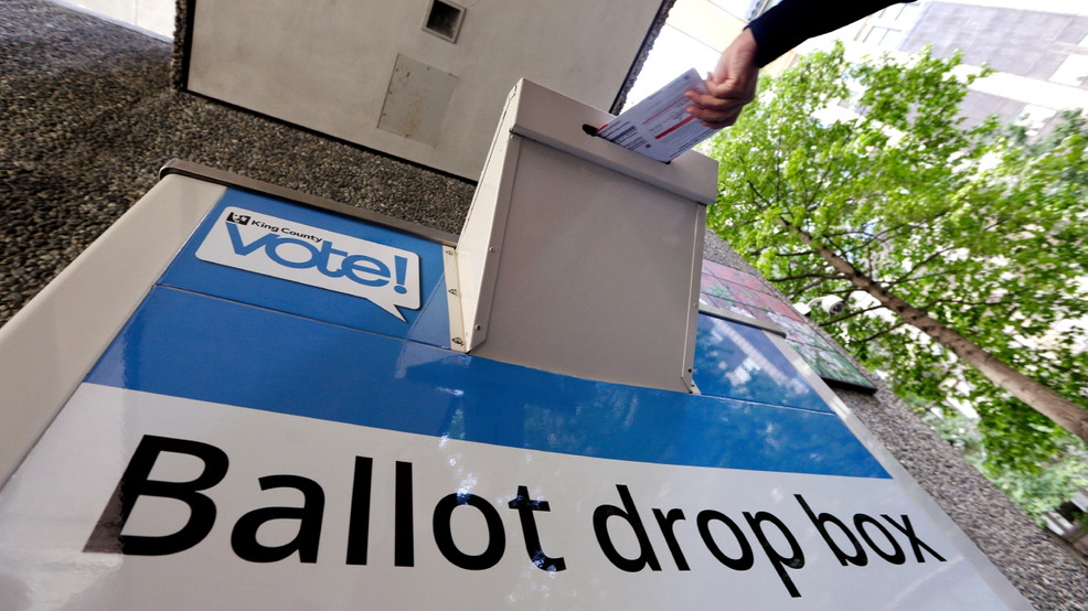 (Hand placing a ballot in dropbox. Photo credit KOMO News)