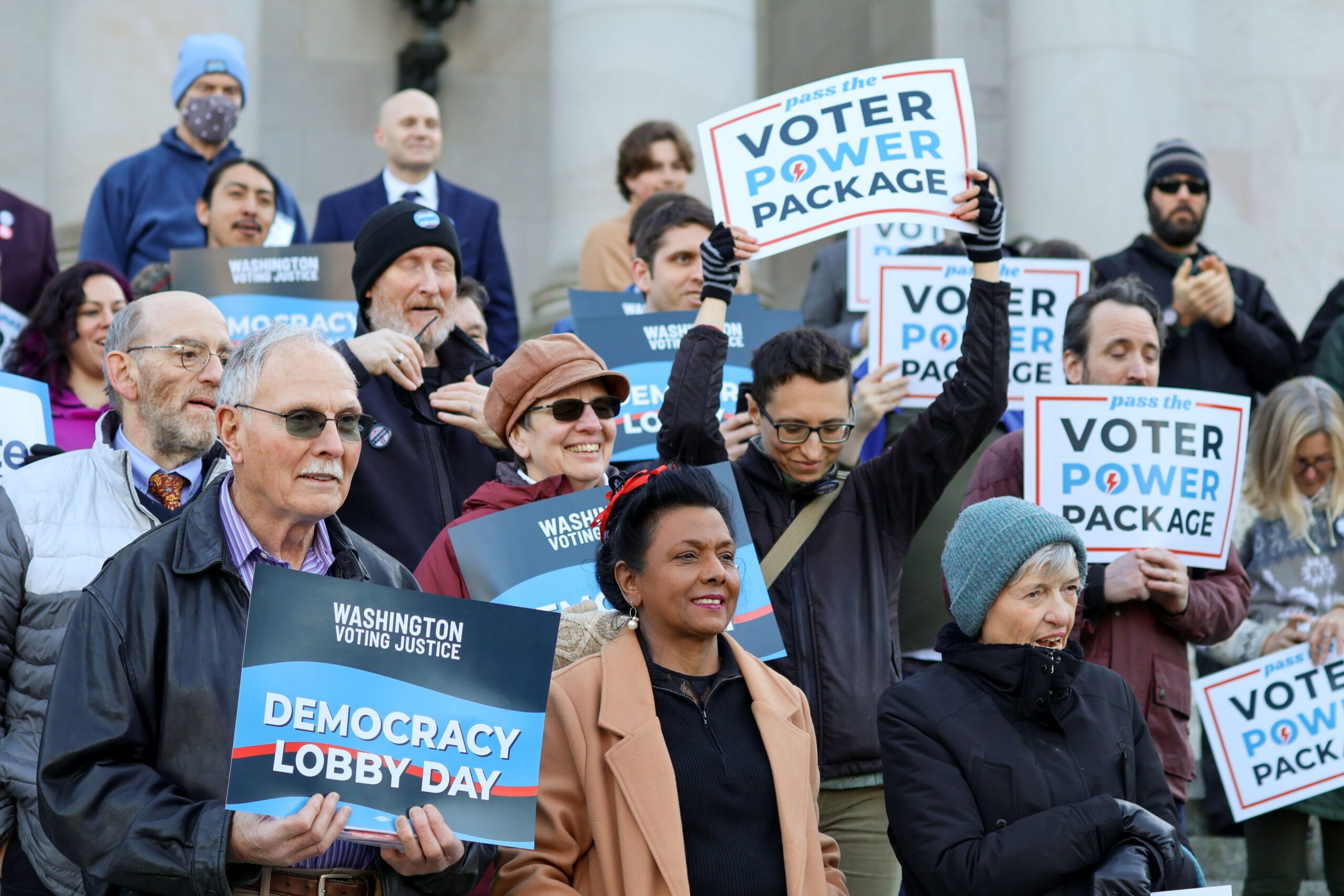Group of event attendees smile and hold up "Democracy Lobby Day" and "Voter Power Package" signs