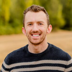 A man wears a striped sweater and smiles at the camera.